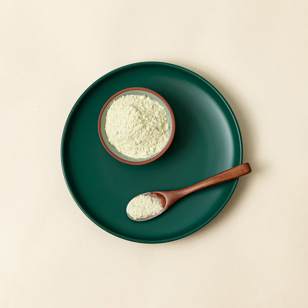 A wooden spoon and a small dish containing wasabi powder, both are on top of a round green dinner plate.