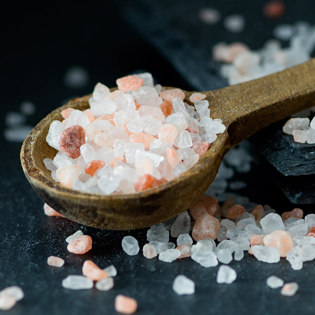A teaspoon of Soeos Himalayan Pink Salt, and some pink salt in the background. 